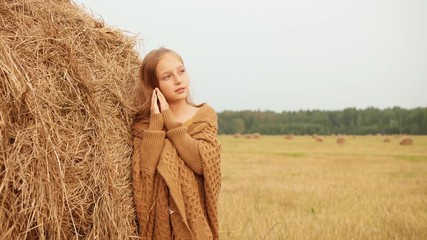 adorable happy girl posing near haystack in field. beautiful smiling teenage girl with long hair lea