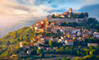 Antique city Motovun Croatia Istria. Picturesque panorama age-old village at hill with pink cloud and sunny light and authentic home with red tegular roof and green vineyard garden.
