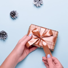 Woman with blue manicure holding craft paper gift box or wrapped present on blue background with painted silver pine cones and confetti. Christmas presents or shopping concept. Top view