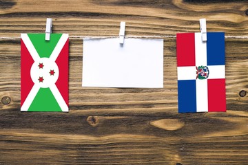 Hanging flags of Burundi and Dominican Republic attached to rope with clothes pins with copy space on white note paper on wooden background.Diplomatic relations between countries.