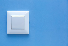 A Light Switch, A Plastic Mechanical Button Of White Color Installed On A Light Blue Wall With Copy Space.