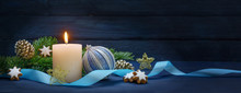 Burning Candle, Fir Branches With Cones And Cinnamon Stars, Blue Christmas Bauble And A Ribbon, As A Festive Decoration Against A Dark Blue Wooden Background With Copy Space, Panoramic Format