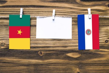 Hanging flags of Cameroon and Paraguay attached to rope with clothes pins with copy space on white note paper on wooden background.Diplomatic relations between countries.