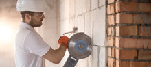 The Industrial Builder Works With A Professional Angle Grinder To Cut Bricks And Build Interior Walls. Electrician.