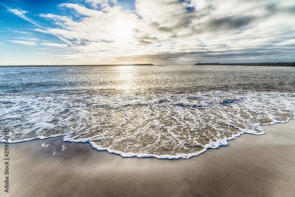 Beautiful shot of the ocean water arriving the shore and the cloudy sky in the background - obrazy, fototapety, plakaty 