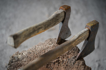 two old axes stuck in a wood block, close up, blurry background