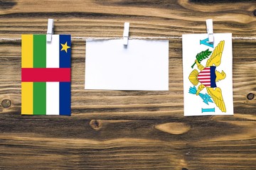 Hanging flags of Central African Republic and United States Virgin Islands attached to rope with clothes pins with copy space on white note paper on wooden background.Diplomatic relations.