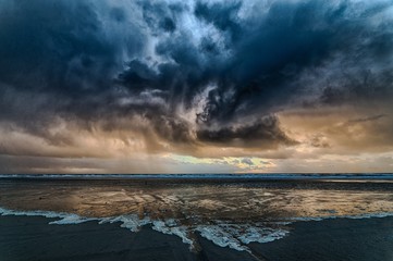 Wall Mural - Breathtaking shot the ocean covered by the dark cloudy sky with the sun hidden behind the clouds