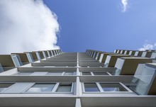 Low Angle Shot Of A Tall White Building With Glass Balconies Under The Clear Blue Sky