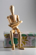 Wooden Pose Doll With Crossed Arms Sitting On A Floral Box