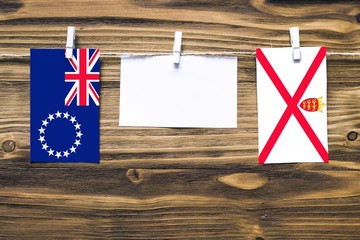 Wall Mural - Hanging flags of Cook Islands and Jersey attached to rope with clothes pins with copy space on white note paper on wooden background.Diplomatic relations between countries.