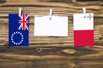 Wall Mural - Hanging flags of Cook Islands and Malta attached to rope with clothes pins with copy space on white note paper on wooden background.Diplomatic relations between countries.