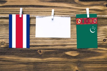 Hanging flags of Costa Rica and Turkmenistan attached to rope with clothes pins with copy space on white note paper on wooden background.Diplomatic relations between countries.