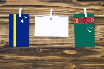 Hanging flags of Curacao and Turkmenistan attached to rope with clothes pins with copy space on white note paper on wooden background.Diplomatic relations between countries.