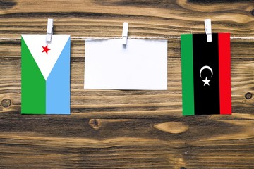 Wall Mural - Hanging flags of Djibouti and Libya attached to rope with clothes pins with copy space on white note paper on wooden background.Diplomatic relations between countries.