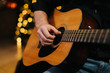 © dikushin - Man plays guitar close-up. Against the background of a decorated Christmas tree with a bokeh effect.