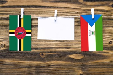 Hanging flags of Dominica and Equatorial Guinea attached to rope with clothes pins with copy space on white note paper on wooden background.Diplomatic relations between countries.