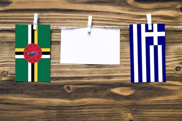 Hanging flags of Dominica and Greece attached to rope with clothes pins with copy space on white note paper on wooden background.Diplomatic relations between countries.