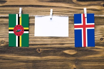 Hanging flags of Dominica and Iceland attached to rope with clothes pins with copy space on white note paper on wooden background.Diplomatic relations between countries.