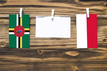 Hanging flags of Dominica and Indonesia attached to rope with clothes pins with copy space on white note paper on wooden background.Diplomatic relations between countries.