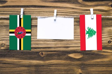 Hanging flags of Dominica and Lebanon attached to rope with clothes pins with copy space on white note paper on wooden background.Diplomatic relations between countries.