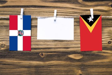 Hanging flags of Dominican Republic and East Timor attached to rope with clothes pins with copy space on white note paper on wooden background.Diplomatic relations between countries.