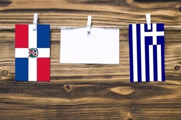 Hanging flags of Dominican Republic and Greece attached to rope with clothes pins with copy space on white note paper on wooden background.Diplomatic relations between countries.