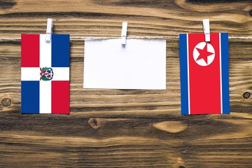 Hanging flags of Dominican Republic and North Korea attached to rope with clothes pins with copy space on white note paper on wooden background.Diplomatic relations between countries.