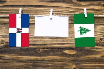 Hanging flags of Dominican Republic and Norfolk Island attached to rope with clothes pins with copy space on white note paper on wooden background.Diplomatic relations between countries.