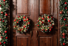 House Entrance Decorated For Holidays. Christmas Decoration. Two Wreaths And Garland Of Fir Tree Branches. Large Wooden Door