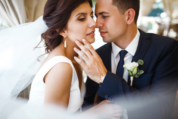 Young bride and groom in a cafe. Husband and wife hold each other's hands. Loving couple in a restaurant. Groom kissing a bride. Pretty bride and stylish groom. Wedding day. Marriage.