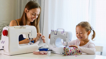 Mother and daughter is sewing on a machine. A woman using a needle. A mother and a daughter are spending time at home together, day time.