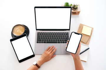 top view mockup image of hands holding a blank white screen mobile phone with laptop computer and ta