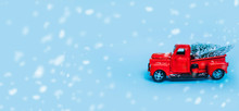 Red Truck Car Carrying A Christmas Fir Tree With Garland On The Snow Blue Background. Concept For Magic Fairytale Merry Christmas And Winter Holidays. Copy Space Place Text. Snow Bokeh