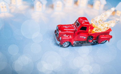 Red truck car carrying a Christmas fir tree with garland on the snow blue background. Concept for magic fairytale Merry Christmas and Winter holidays. Copy space Place text. Snow bokeh