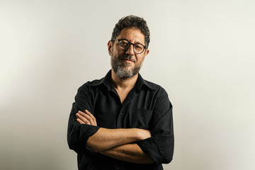 Portrait of a mid age bearded man wearing glasses with hands crossed on a clean neutral background