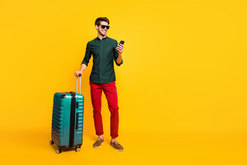 Canvas Print - Full size profile side photo of cheerful traveler guy on summer vacation reach destination hold package use cellphone reserve taxi wear green shirt pants trousers isolated yellow color background