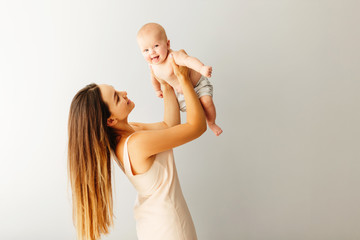 Wall Mural - beautiful happy mother holds her baby on a plain light background.