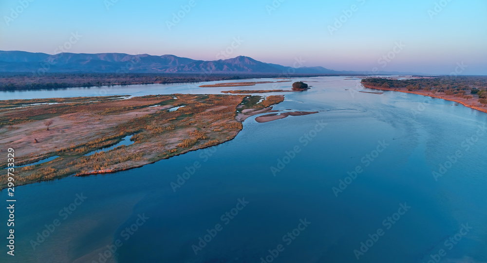 Aerial, east view of Zambezi river during sunset. View on african wilderness, mountains and huge river Zambezi from above. Border river. UNESCO Heritage Site, Mana Pools National Park, Zimbabwe. - obrazy, fototapety, plakaty 