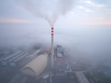 Smoking Chimney Of A Power Plant Coming Out Of The Inverse Fog. The Power Plant Chimney In Operation, A Red-white Striped, Rises Above The Surrounding Fog. Energy Industry. Heating Plant In Operation.