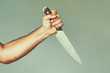 Hand of caucasian man holding a knife isolated on a gray background. Man hold knife - aggression. Big kitchen knife in man hand. Large kitchen knife in a man's hand.  