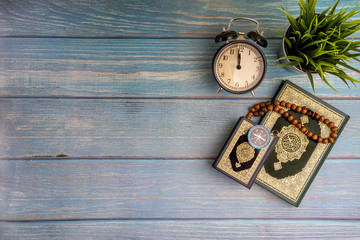 Poster - Flat lay view of vase, tasbih or rosary beads, compass, clock and Holy book of Al Quran with arabic calligraphy meaning of Al Quran over wooden background. Selective focus and crop fragment