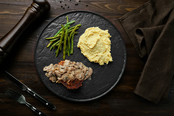 Wall Mural - Salisbury Steak with Onion-Mushroom Gravy, Smashed Potatoes and Green Beans served on a back plate with a fork and a knife. Top view, directly above.