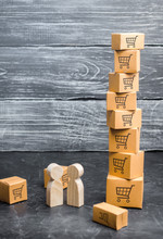 Two Wooden People Stand Near A Tower Of Boxes. Buyer And Seller, Manufacturer And Retailer. Business And Commerce. Discussion Of The Terms Of The Trading Deal, The Purchase Of Goods And Services.
