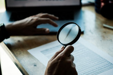 Businessman Looking Through A Magnifying Glass To Documents. Business Assessment And Audit. Magnifying Glass On A Financial Report. Concept Of Search.