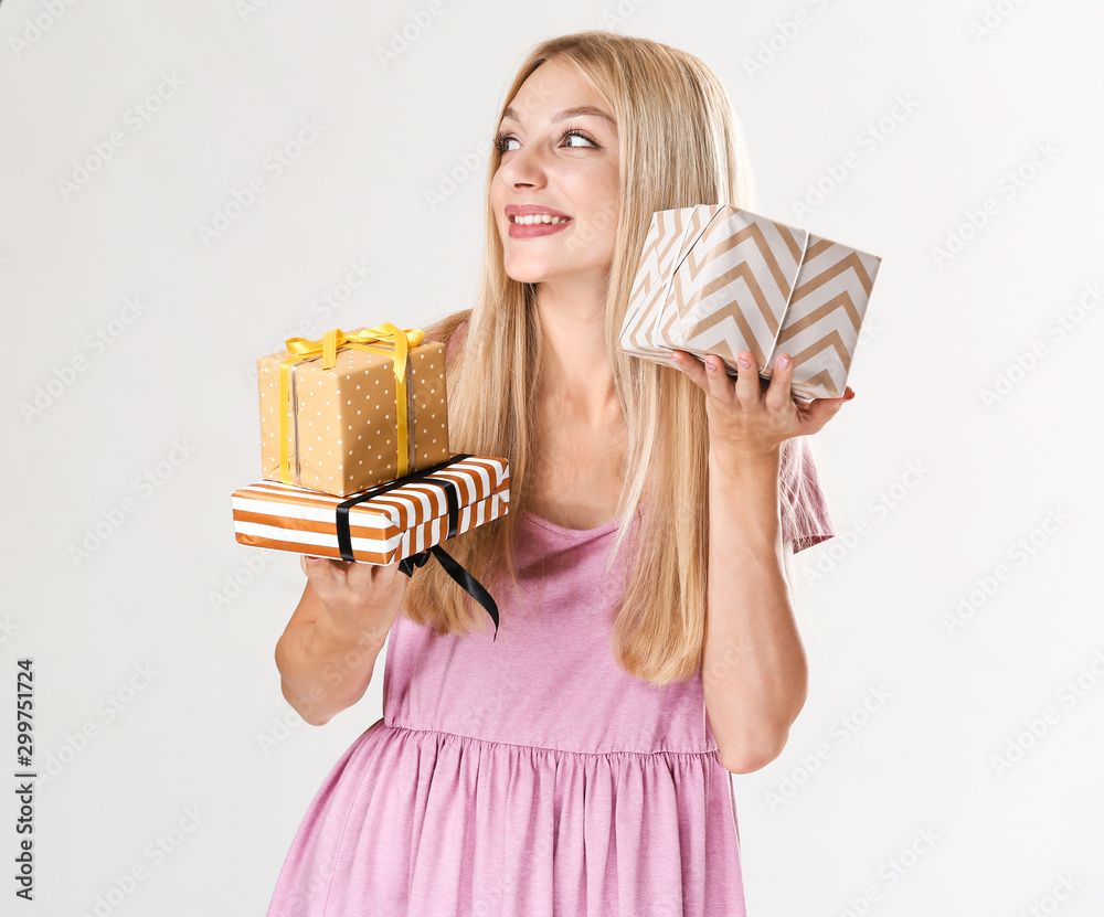 Beautiful young woman with gifts on light background