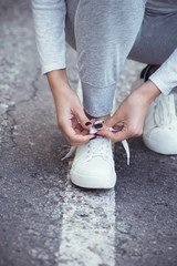  girl squatted down to tie shoelaces on white sneakers on asphalt road, autumn sport concept outdoors