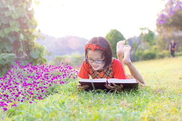 Canvas Print - Cute little girl with glasses reading book at flowers park in summer sunset light