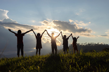 Silhouette group of happy children playing on mountain at sunset, summer time