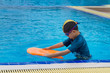 5 years old Lonely boy warm up with orange swimming kickboard before learning to swim in the blue swimming pools.